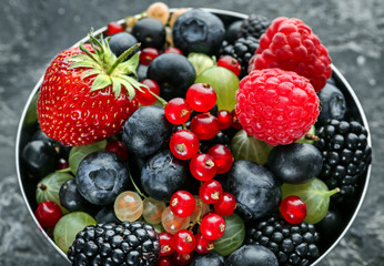 Bowl with delicious ripe berries on grey textured background, closeup