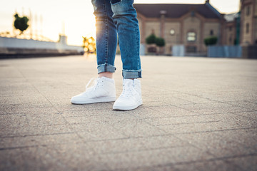 High tops. Girl in blue jeans and white sport shoes standing on the ground