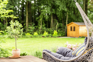 Hammock chair with striped cushion placed on terrace outside the house with garden