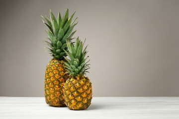 Delicious pineapples on wooden table  against grey background