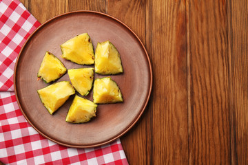 Plate with pieces of ripe pineapple on wooden background