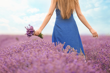 Beautiful young woman with bouquet of lavender in field on summer day