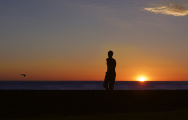 Fototapeta premium Silhouette of the running man on sunset sun. Man near the sea. Happy man. Silhouette of guy on sunset. Unknown man on sunset. Sunset. Summer holidays 