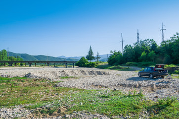 Road trip on car. A car standing near the river on a pebble rocks in the mountains. Wild nature background