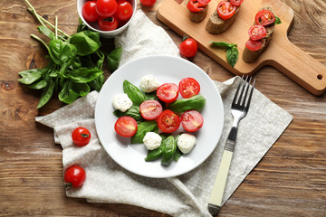 Plate with fresh ripe cherry tomatoes, basil and mozzarella on wooden table
