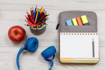 Headphones, apple, metal stand with color pencils and open exercise book on bag-pencil case with...