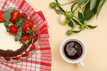 Homemade chocolate cake decorated with fresh strawberries on glass plate, cup of coffee and bouquet of peonies