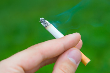 Cigarette in the hand with smoke on a green background