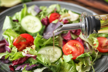 Adding of olive oil to tasty vegetable salad, closeup