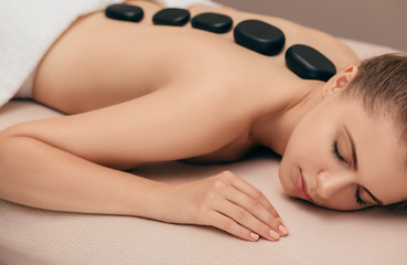 fresh beautiful woman lying on massage table receiving hot stones treatment at spa salon. Hot stone massage treatment