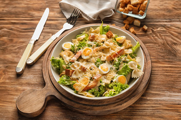 Tasty Caesar salad with pasta in bowl on wooden table
