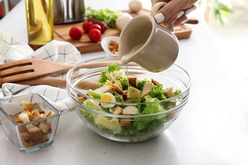 Woman adding sauce to delicious Caesar salad with pasta on table