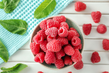 Bowl with delicious fresh ripe raspberries on white wooden table