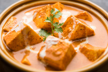 Paneer Butter Masala also known as Panir  makhani or makhanwala. served in a ceramic or terracotta bowl with fresh cream and coriander. Isolated over colourful moody background. selective focus