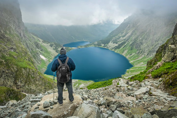 A man with trekking poles and backpack staying and looking at Czarny Staw pod Rysami and Morskie Oko lakes in Tatra Mountains