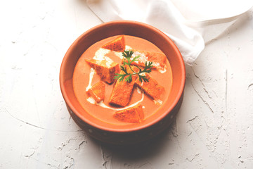 Paneer Butter Masala also known as Panir  makhani or makhanwala. served in a ceramic or terracotta bowl with fresh cream and coriander. Isolated over colourful moody background. selective focus