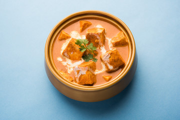 Paneer Butter Masala also known as Panir  makhani or makhanwala. served in a ceramic or terracotta bowl with fresh cream and coriander. Isolated over colourful moody background. selective focus