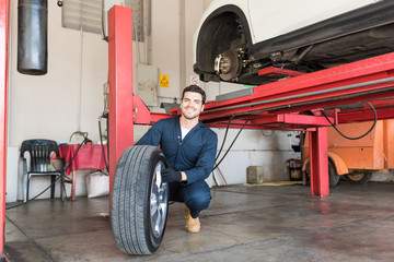 Mechanic Examining Car Tire While Crouching In Workshop