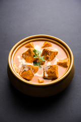 Paneer Butter Masala also known as Panir  makhani or makhanwala. served in a ceramic or terracotta bowl with fresh cream and coriander. Isolated over colourful moody background. selective focus