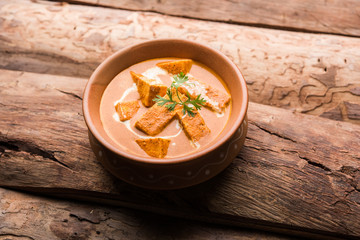 Paneer Butter Masala also known as Panir  makhani or makhanwala. served in a ceramic or terracotta bowl with fresh cream and coriander. Isolated over colourful moody background. selective focus