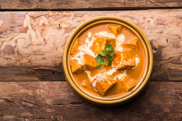 Paneer Butter Masala also known as Panir  makhani or makhanwala. served in a ceramic or terracotta bowl with fresh cream and coriander. Isolated over colourful moody background. selective focus