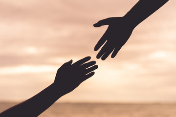 silhouette helping hands on blurred sea and sky background. Friendship Day concept.
