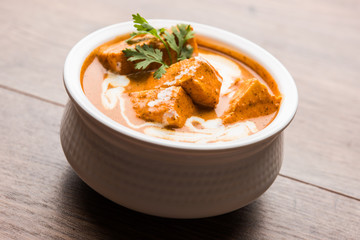 Paneer Butter Masala also known as Panir  makhani or makhanwala. served in a ceramic or terracotta bowl with fresh cream and coriander. Isolated over colourful moody background. selective focus
