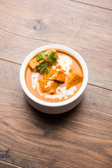 Paneer Butter Masala also known as Panir  makhani or makhanwala. served in a ceramic or terracotta bowl with fresh cream and coriander. Isolated over colourful moody background. selective focus
