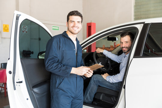 Smiling Mechanic Standing By Customer In Car At Garage