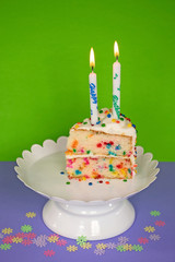 slice of birthday cake with candle on white pedestal plate and confetti