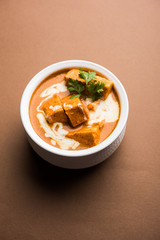 Paneer Butter Masala also known as Panir  makhani or makhanwala. served in a ceramic or terracotta bowl with fresh cream and coriander. Isolated over colourful moody background. selective focus