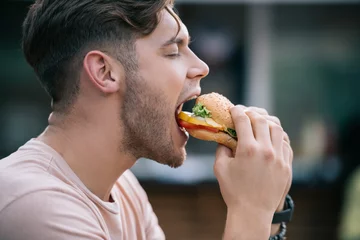 Foto op Plexiglas side view of man eating tasty burger with closed eyes © LIGHTFIELD STUDIOS