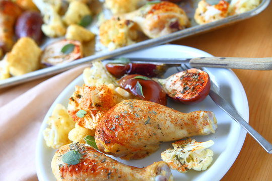 Plate of roasted chicken legs, mini eggplants and cauliflower seasoned with dried herbs and smoked paprika