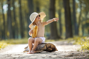 Young beautiful toddler girl sitting on a wooden log eating bread
