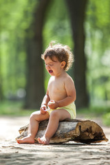 Young beautiful toddler girl sitting on a wooden log crying