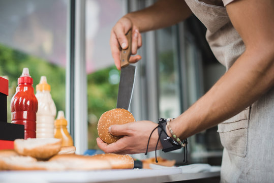 cropped image of chef cutting bun with knife in food truck