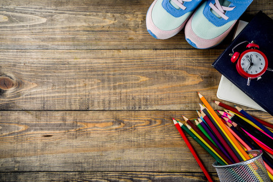 Back to school concept with kids sneakers, books, color pencils and alarm clock, wooden desk background top view copy space
