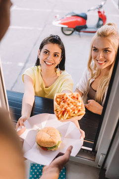 cropped image of chef giving burger and french fries to smiling customers from food truck