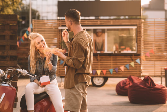 happy couple eating french fries and burger near food truck