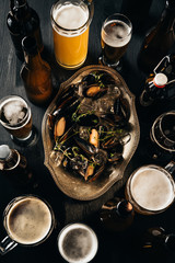 top view of arrangement of beer and mussels with ice cubes on dark wooden tabletop