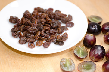 Grapes with raisins on a plate on wooden background