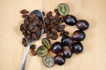 Spoonful of raisins with red grapes on wooden background