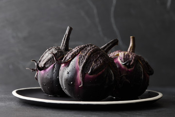 Fresh Italian type eggplants or aubergines with water drops in black plate on dark stone background