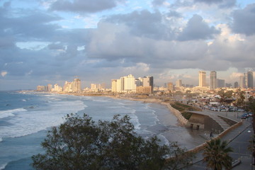 Panorama of the skyscrapers of the city of Tel Aviv near the shores of the Mediterranean, covered with winter waves, and against the background of the cloudy sky with little clarification.