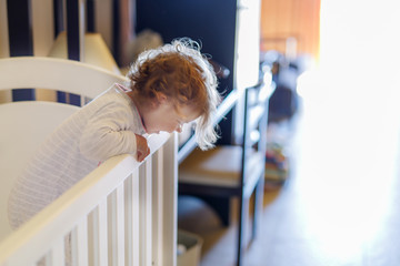 Cute little baby girl lying in cot after sleeping. Healthy happy child in bed climbing out.