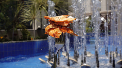 Fried meat, chicken meat, against a background of a fountain. The food on the fork is spinning.