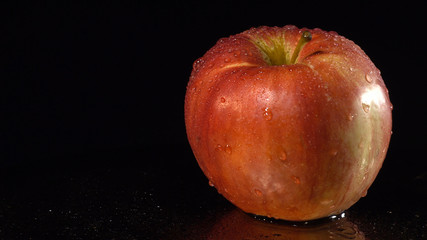 Ripe red apple on a mirror background. A red apple rotates on a wet mirror. Food concept.