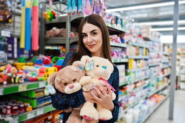 Shopping woman looking at the shelves in the supermarket.  Portrait of a young girl in a market store holding small soft toys.