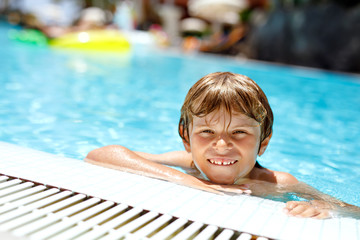 Portrait of happy little kid boy in the pool and having fun on family vacations in a hotel resort. Healthy child playing in water