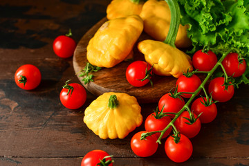 organic yellow patissons with cherry tomatoes and salad on a wooden table. a new harvest of vegetables from the garden, vegan food, a diet food. selective focus and copy space